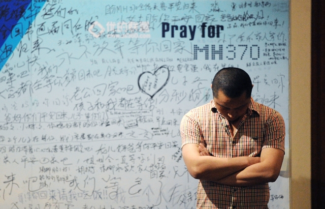 A man stands in front of a billboard in support of missing Malaysia Airlines flight MH370