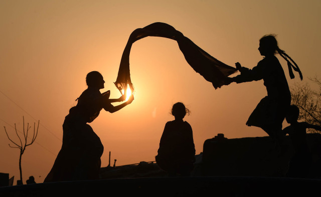 Pakistani girls are silhouetted as they play at a slum area of Lahore on March 4, 2015. AFP PHOTO/ ARIF ALI