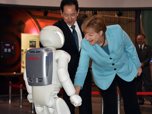 German Chancellor Angela Merkel shakes hands with Japanese auto giant Honda Motor's humanoid robot Asimo as museum head and former astronaut Mamoru Mori looks on at the National Museum of Emerging Science and Innovation in Tokyo on March 9, 2015. Merkel went on a two day visit to Tokyo for talks with Shinzo Abe. AFP / Yoshikazu Tsuno