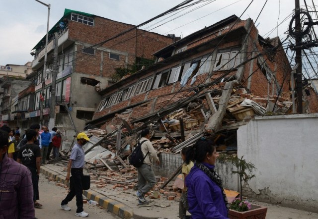 TOPSHOTS Nepalese people walk past a collapsed bullding in Kathmandu after an earthquake on April 25, 2015. A massive 7.8 magnitude earthquake killed hundreds of people April 25 as it ripped through large parts of Nepal, toppling office blocks and towers in Kathmandu and triggering a deadly avalanche that hit Everest base camp. AFP PHOTO / PRAKASH MATHEMA