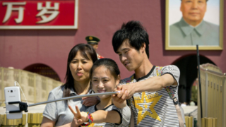 Tourists use a selfie stick to take a photo of themselves in front of a large portrait of late Chinese leader Mao Zedong on the Gate of Heavenly Peace near Tiananmen Square in Beijing, Sunday, May 3, 2015. Millions of Chinese are taking advantage of the May Day holidays to visit popular tourist sites. (AP Photo/Mark Schiefelbein)