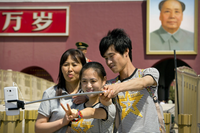 Tourists use a selfie stick to take a photo of themselves in front of a large portrait of late Chinese leader Mao Zedong on the Gate of Heavenly Peace near Tiananmen Square in Beijing, Sunday, May 3, 2015. Millions of Chinese are taking advantage of the May Day holidays to visit popular tourist sites. (AP Photo/Mark Schiefelbein)