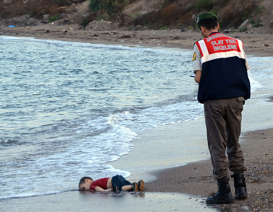 A paramilitary police officer investigates the scene before carrying the lifeless body of Aylan Kurdi, 3, after a number of migrants died and a smaller number were reported missing after boats carrying them to the Greek island of Kos capsized, near the Turkish resort of Bodrum early Wednesday, Sept. 2, 2015. (AP Photo/DHA)