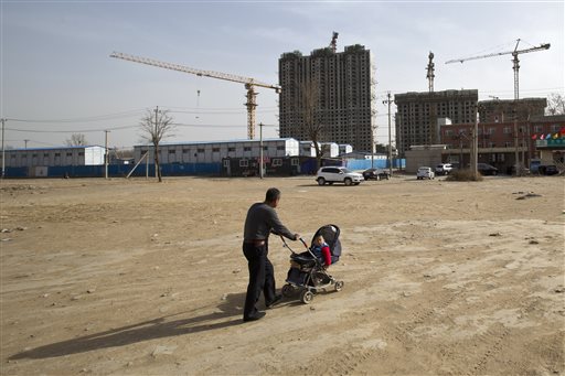 FILE - In this Monday, March 17, 2014, file photo, a man pushes a baby buggy near a construction site of a residential real estate project in a village on the outskirts of Beijing. (AP Photo/Alexander F. Yuan, File)
