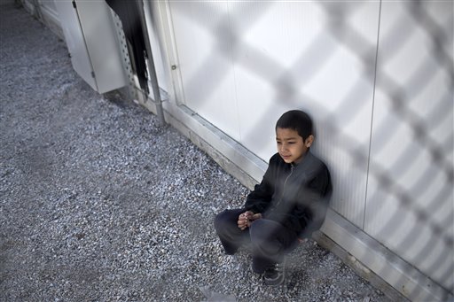 A boy sits inside an enclosure at the migrant and refugee registration camp in Moria, on the island of Lesbos, Greece, Thursday, Nov. 5, 2015.  The European Union predict that around 3 million more migrants are expected to arrive in the 28-nation bloc by the end of next year. (AP Photo/Marko Drobnjakovic)