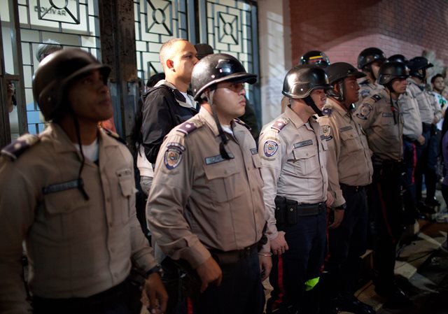 National police officers lineup in front of the main entrance of a polling station as pro-government supporters demand that the polling station reopen, during congressional elections in Caracas, Venezuela, Sunday, Dec. 6, 2015. Some members of the opposition are angry after elections officials ordered polling centers to stay open for an extra hour, even if no one was standing in line to vote. Government opponents mobbed some voting stations demanding that the National Guard stick to the original schedule of closing at 6 p.m. (AP Photo/Alejandro Cegarra)