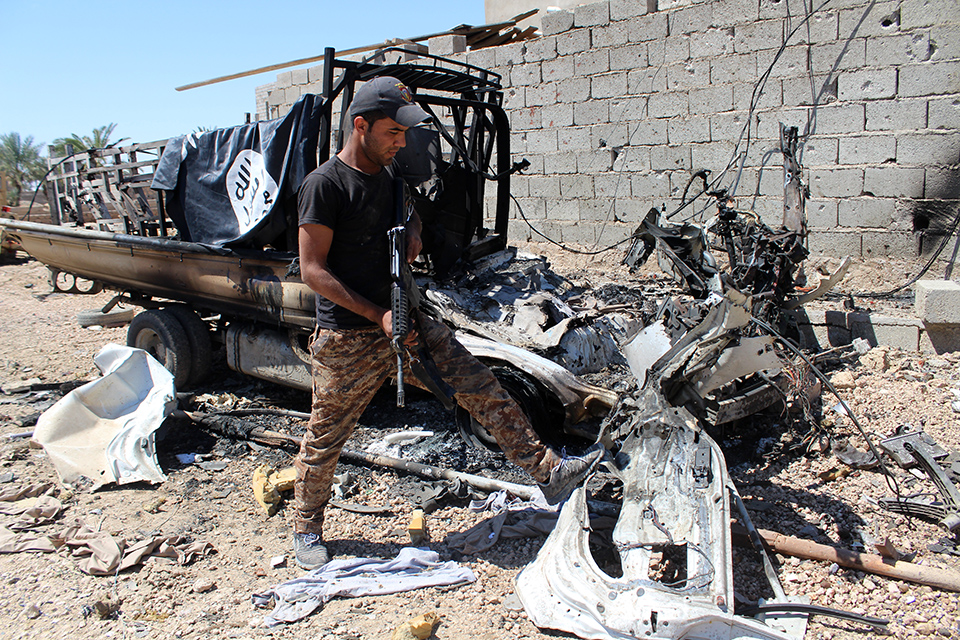 A member of Iraqi government forces inspects a burnt vehicle with on its top a flag of the Islamic State group (IS) after they retook an area from its jihadists on April 2, 2016 in the village of Al-Mamoura, near Heet, a Euphrates Valley town located about 145 kilometres west of Baghdad in the western province of Anbar. (AFP / MOADH AL-DULAIMI)