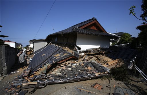 A resident walks by a collapsed house in Mashiki, Kumamoto prefecture, southern Japan, Friday, April 15, 2016. Aftershocks rattled communities in southern Japan as businesses and residents got a fuller look Friday at the widespread damage from an unusually strong overnight earthquake. (AP Photo/Koji Ueda)