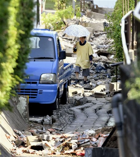 A resident walks through the debris after a magnitude-6.5 earthquake in Mashiki, Kumamoto prefecture, southern Japan, Friday, April 15, 2016. More than 100 aftershocks from Thursday night's earthquake continued to rattle the region as businesses and residents got a fuller look at the widespread damage from the unusually strong quake, which also injured about 800 people. (Kyodo News via AP)