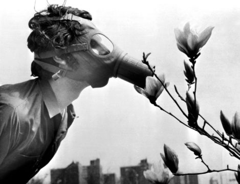 Woman in a gas mask smelling flowers.