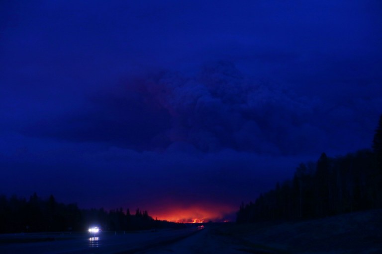 A plume of smoke hangs in the air as forest fires rage on in the distance in Fort McMurray, Alberta on May 4, 2016. Numerous vehicles can be seen abandoned on the highways leading from the raging forest fires in Fort McMurray and neighbouring communities have banded together to offer support in the form of food, water, and gasoline. / AFP PHOTO / Cole Burston
