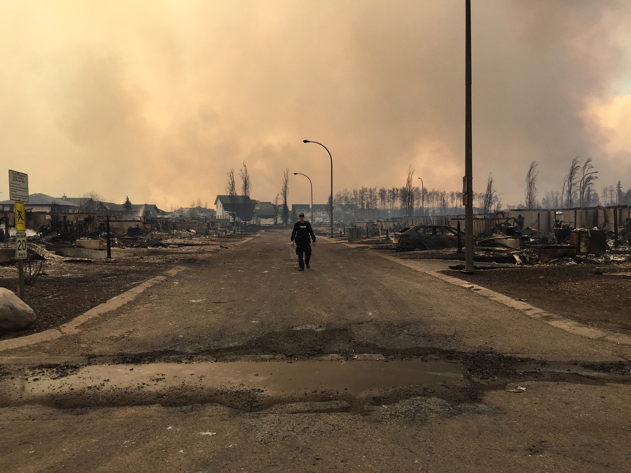 In this image released by the Alberta RCMP on May 5, 2016, a police officer walks on a road past burned down houses in Fort McMurray, Alberta. Canada prepared to airlift to safety up to 25,000 people who were forced from their homes by raging forest fires in Alberta's oil sands region, and now risk getting trapped north of Fort McMurray. / AFP PHOTO / Alberta RCMP / RCMP / RESTRICTED TO EDITORIAL USE - MANDATORY CREDIT "AFP PHOTO / ALBERTA RCMP/ HO" - NO MARKETING NO ADVERTISING CAMPAIGNS - DISTRIBUTED AS A SERVICE TO CLIENTS