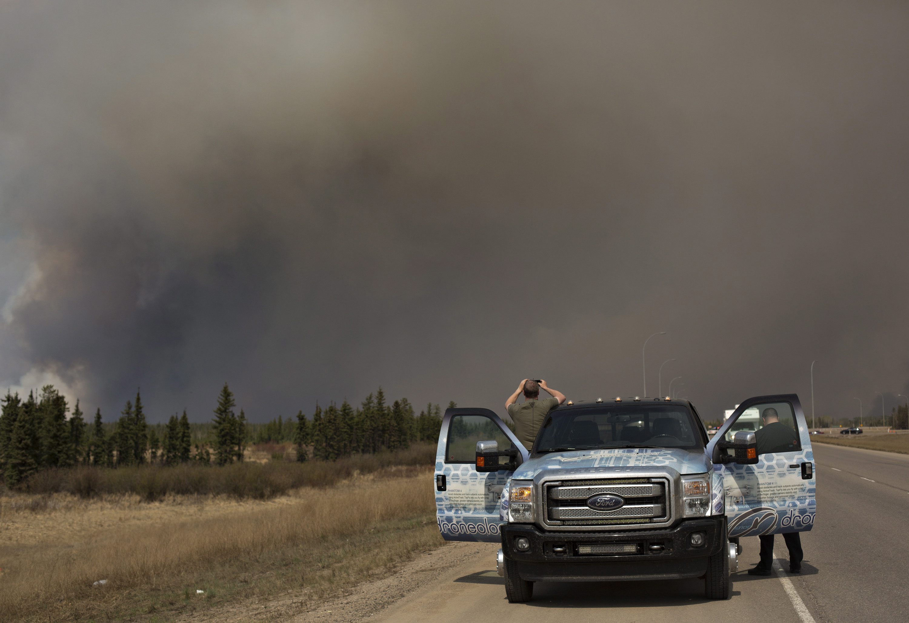 People stop to take photos of a wildfire south of Fort McMurray, Alberta, Canada on Thursday May 5, 2016. Raging wildfires in the Canadian province of Alberta have moved south, forcing three more communities to evacuate and an emergency operations center to move again. (Jason Franson/The Canadian Press via AP) MANDATORY CREDIT