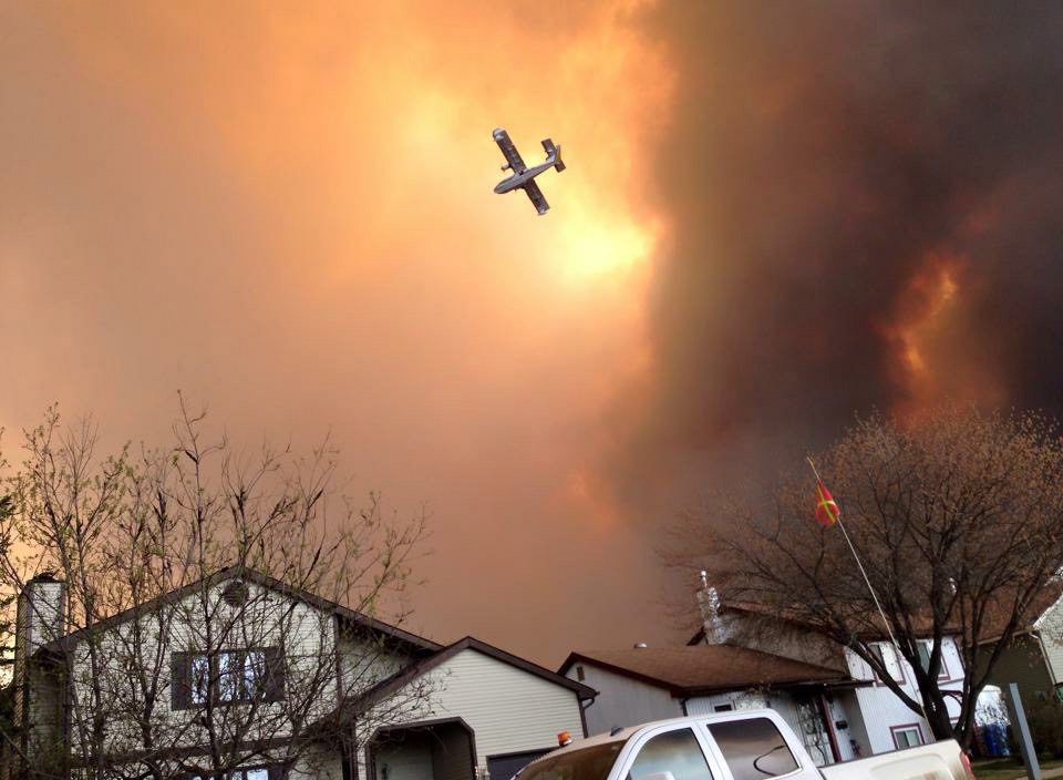 Smoke fills the air as a small plane flies overhead in Fort McMurray, Alberta, Tuesday, May 3, 2016. The entire population of the Canadian oil sands city of Fort McMurray, has been ordered to evacuate as a wildfire whipped by winds engulfed homes and sent ash raining down on residents. (Kitty Cochrane/The Canadian Press via AP) MANDATORY CREDIT