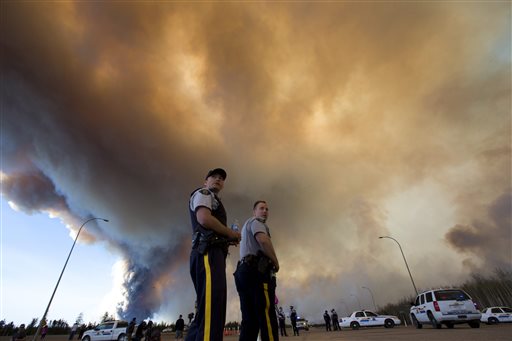 Police officers direct traffic under a cloud of smoke from a wildfire in Fort McMurray, Alberta, Canada on Friday, May 6, 2016. Tens of thousands have been forced from their homes, and the fires are expected to burn for weeks. (Jason Franson/The Canadian Press via AP) MANDATORY CREDIT