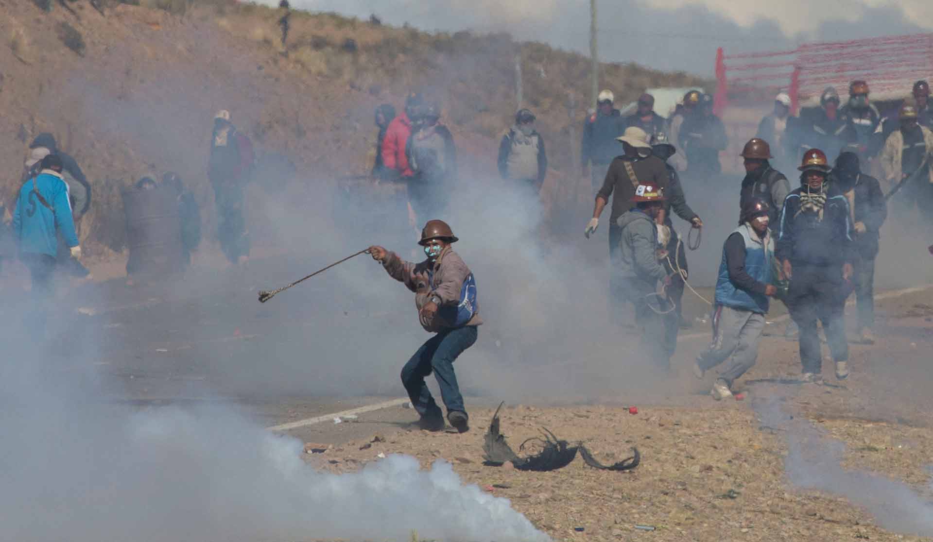 Independent miners clash with the police as they run from clouds of tear gas during protests in Panduro, Bolivia, Thursday, Aug. 25, 2016. Thousands of independent miners continued their protests with roadblocks which precipitated the clashes as the police attempted to dislodge them. (AP Photo/Juan Karita)