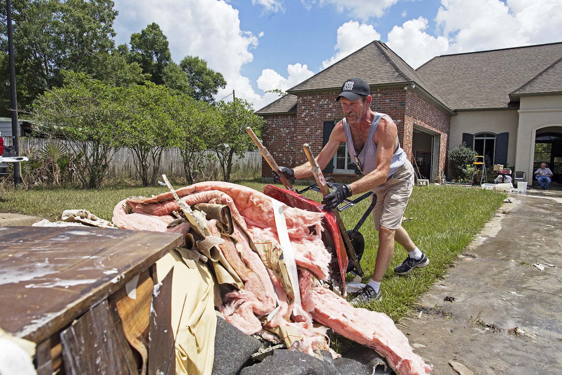 Jody Harelson, 52, dumps a wheel barrel of wet sheet rock an ever growing pile of rubbish as he helps clean out the flood damaged home of Sheila Siener, 58, in St. Amant, La., Saturday, Aug. 20, 2016.  Louisiana continues to dig itself out from devastating floods, with search parties going door to door looking for survivors.  (AP Photo/Max Becherer)
