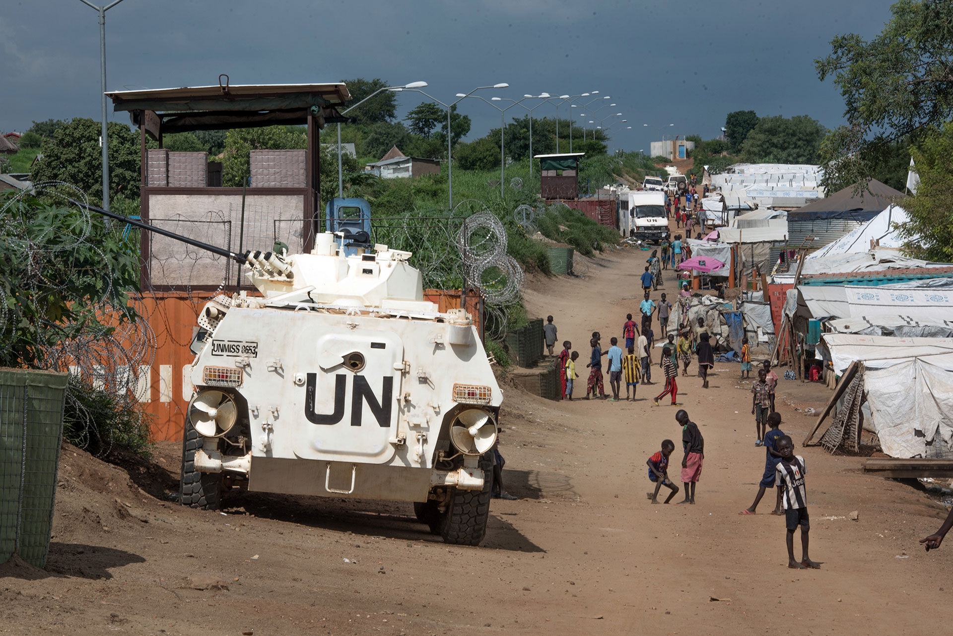 In this  photo taken Monday July. 25, 2016, Some of more than 30,000 Nuer civilians sheltering in a United Nations base in South Sudan's capital Juba for fear of targeted killings by government forces walk by an armored vehicle and a watchtower manned by Chinese peacekeepers. (AP Photo/Jason Patinkin) 