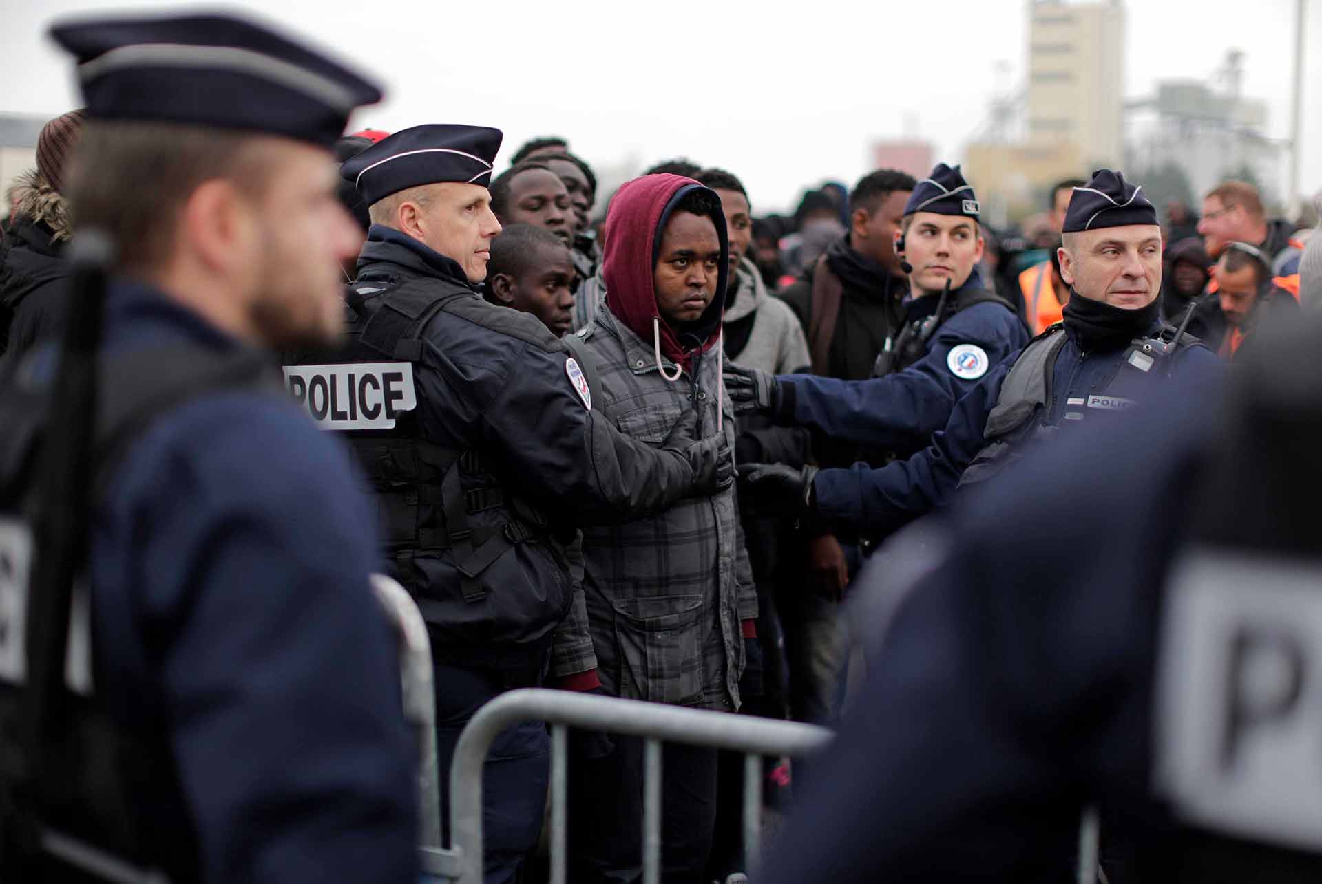 Police officers control a queue as migrants line-up to register at a processing centre in the makeshift migrant camp known as "the jungle" near Calais, northern France, Monday Oct. 24, 2016. (AP Photo/Emilio Morenatti)