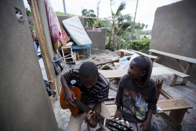 Man sits with guitar aside destroyed home