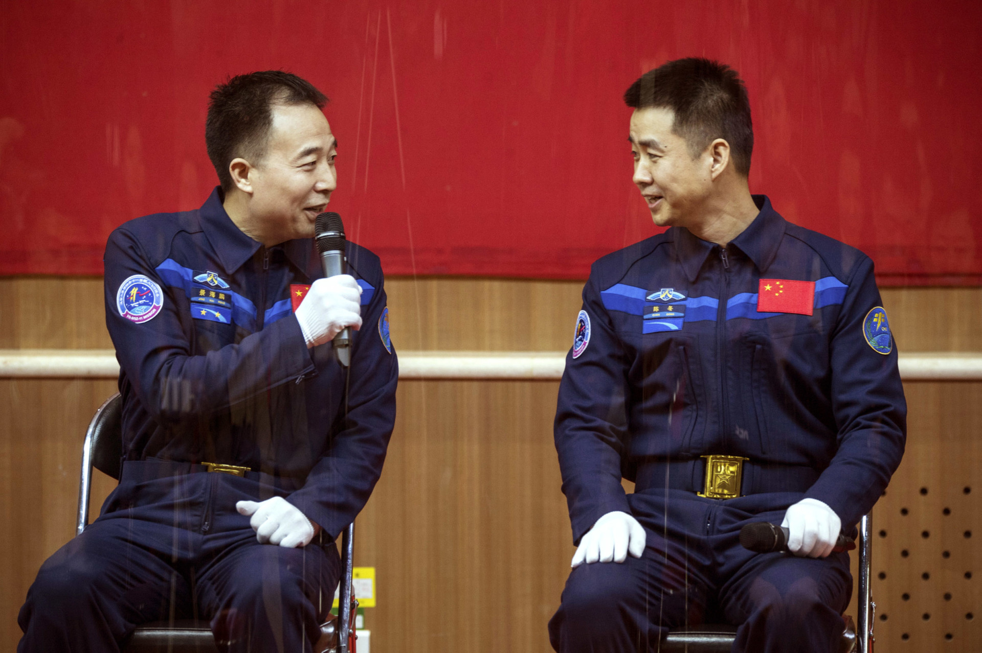 Chinese astronauts Jing Haipeng, left, and Chen Dong, right, chat behind a glass enclosure during a presser at the Jiuquan Satellite Launch Center in northwest China Sunday Oct. 16, 2016. (Chinatopix Via AP)