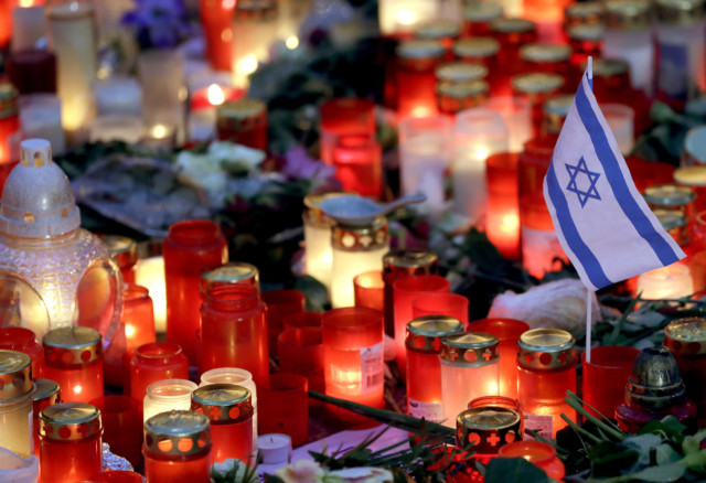 small flag of Israel is pictured between candles and flowers