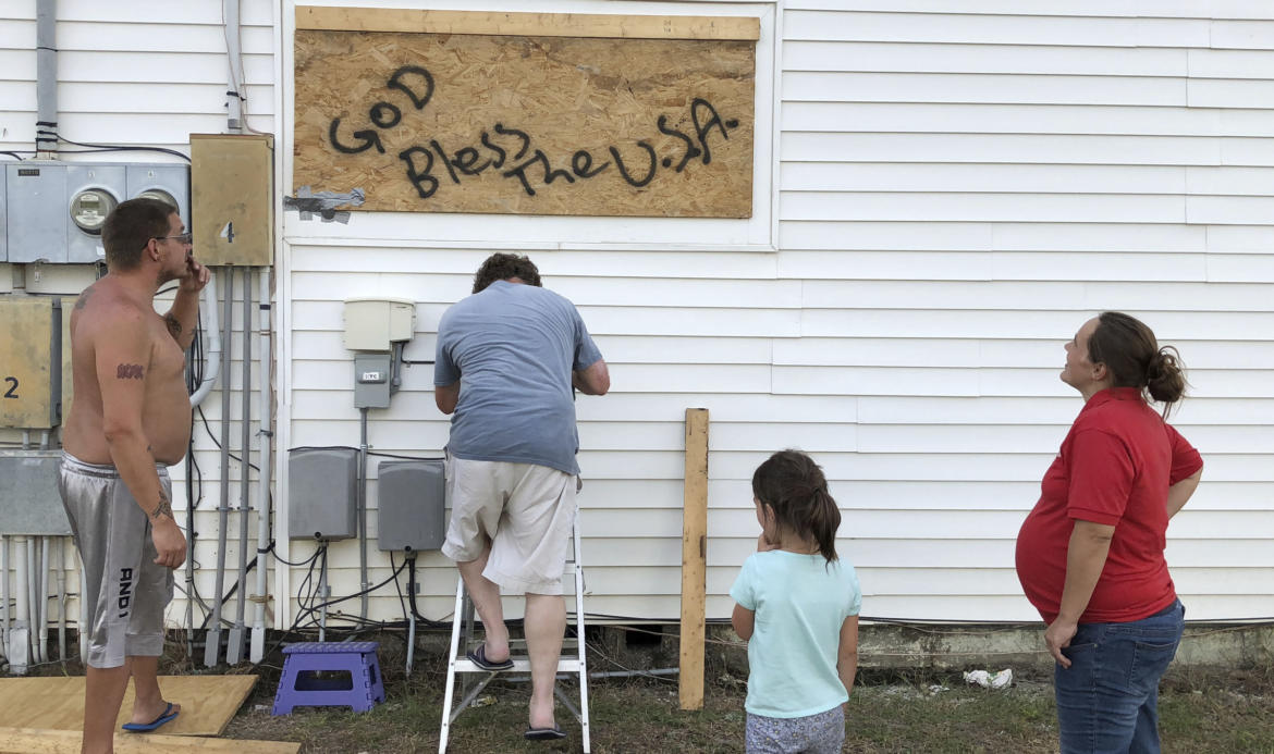 Man nailing plywood sign to house.