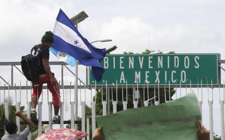 Honduran migrant hold his national flag, climbs the border fence