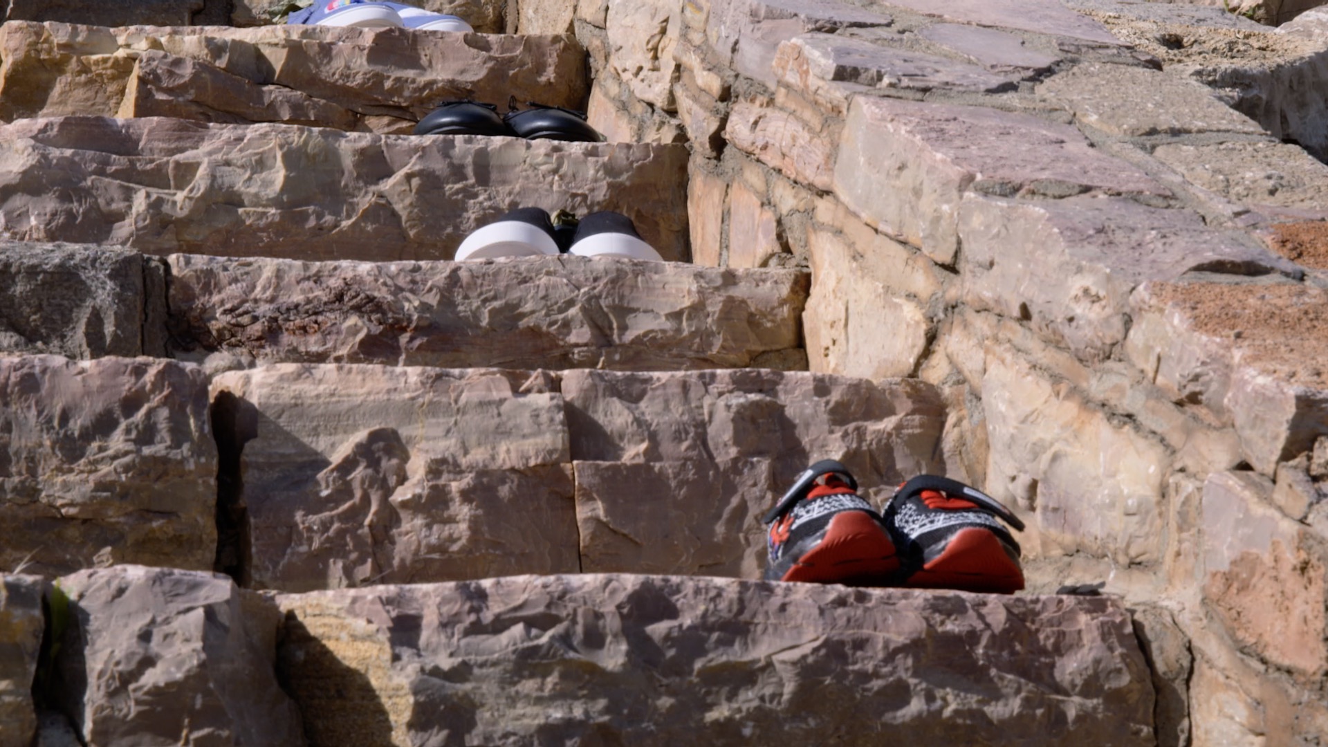 Three pairs of children-sized sneakers on the steps of a stair in brownstone.