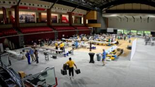 A group of people are setting up a mobile clinic inside the gymnasium of the University of Virginia at Wise. There are gurneys, assorted equipment, and volunteers wearing yellowy T-shirts carrying boxes.