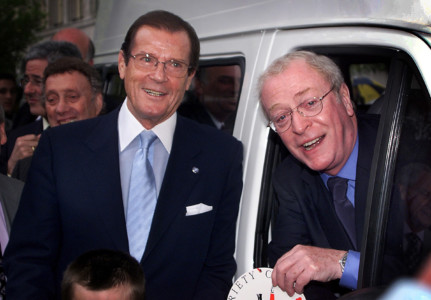 British Oscar winner Michael Caine and Roger Moore (L) pose after presenting a mini-coach to a children's charity in London on April 12, 2000. (PHOTO: AFP PHOTO / ADRIAN DENNIS) Roger Moore