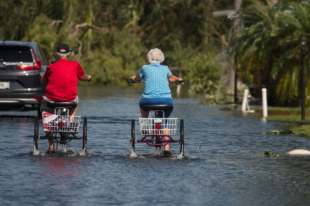 Two retirees ride tricycles through a flooded street at the Enchanted Shores manufactured home park in Naples, Florida, on September 11, 2017 after Hurricane Irma hit Florida. (AFP PHOTO / NICHOLAS KAMM)