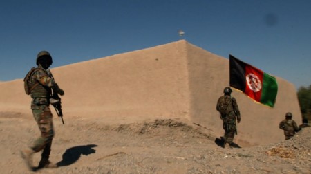 Armed with guns, kevlar and the Afghan flag, troops enter a compound.
