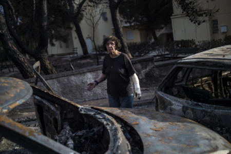 A woman with a cast stands among cars burnt following a wildfire at the village of Mati, near Athens, on July 24, 2018. (AFP PHOTO / ANGELOS TZORTZINIS)