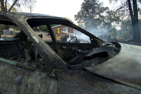 Firefighter Richard Cotter battles a wildfire on Sunday, June 24, 2018, near Clearlake Oaks, Calif. Wind-driven wildfires destroyed buildings and threatened hundreds of others Sunday as they raced across dry brush in rural Northern California. (AP Photo/Noah Berger) Burned vehicle and firefighters hosing