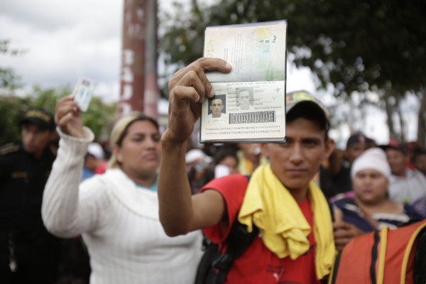Honduran migrant Edwin Antonio Garcia Cruz holds up his passport and the woman behind him holds up her national ID as Guatemalan police block them and their caravan after the group crossed the Honduras-Guatemala border without incident, in Esquipulas, Guatemala, Monday, Oct. 15, 2018. (AP Photo/Moises Castillo) Honduran migrant holds up his passport