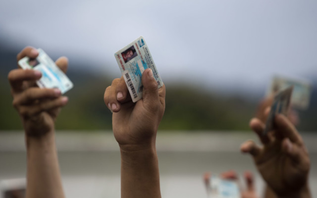 Honduran migrants holds up their national ID cards as Guatemalan police block them and their caravan after the group crossed the Honduras-Guatemala border without incident, in Esquipulas, Guatemala, Monday, Oct. 15, 2018. (AP Photo/Moises Castillo) Honduran migrants holds up their national ID cards