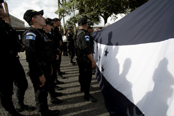 Guatemalan police temporarily block the road where Honduran migrants hold up their national flag after their group crossed the Honduras-Guatemala border without incident, in Esquipulas, Guatemala, Monday, Oct. 15, 2018. (AP Photo/Moises Castillo) Guatemalan police temporarily block the ro