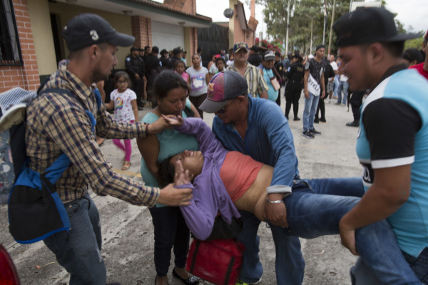 A faint Honduran migrant woman is helped as Guatemalan police temporarily block the road after her caravan crossed the Honduras-Guatemala border without incident, in Esquipulas, Guatemala, Monday, Oct. 15, 2018. Police stopped the migrants for several hours but the travelers refused to return to the border and were eventually allowed to pass. (AP Photo/Moises Castillo) A faint Honduran migrant woman is helped as Guatemalan police temporarily block the road