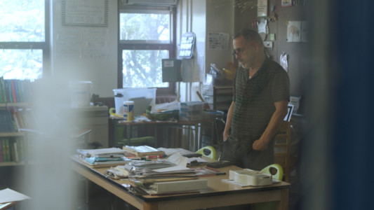 A teacher stands in front of his desk in the classroom.