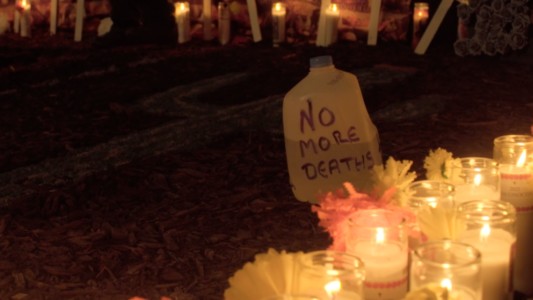 A water jug with "No more deaths" written on it stands between flowers and candlelights remembering the migrant death.