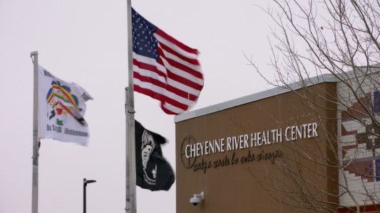 The front of a Health Center, we see the sign on the wall and two flags in the front