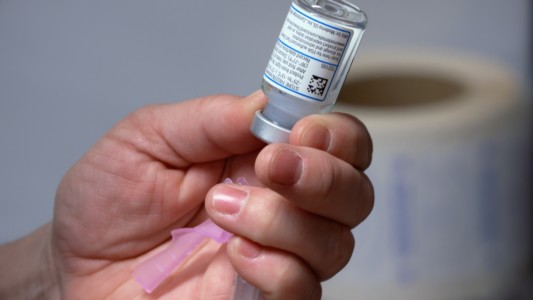 A close up of a hand holding a vial of vaccine and a syringe