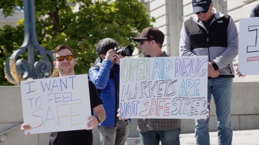 Two people holding signs calling for tougher law enforcement in front of San Francisco City Hall. A photographer is seen on the back.